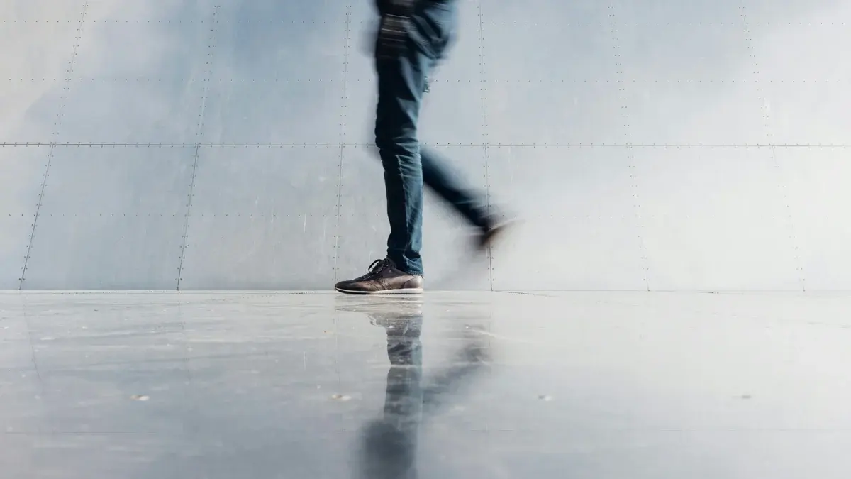A person walking past a silver wall, reflected on the floor